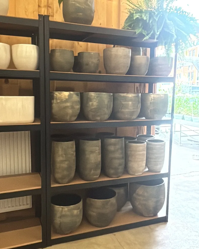 Stellingen vol keramieken potten in oud roze, crème, groen en zwart